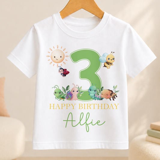 A white t-shirt with a green number 3 and various cartoon insects, including a ladybug, on it. The text below the number reads "Happy Birthday Alfie".