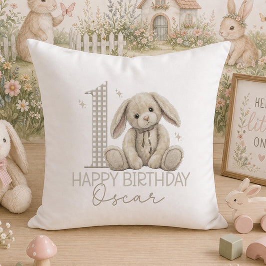 White square cushion printed with a cartoon rabbit, a large number one and the personalised text Happy Birthday Oscar, photographed on a wooden surface