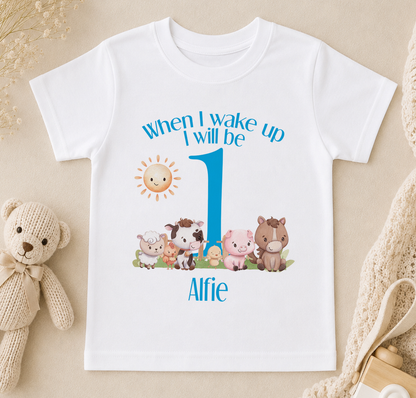 A white t-shirt with a personalized design featuring a cartoon image of farm animals and the text "When I wake up I will be 1" along with the name "Alfie".