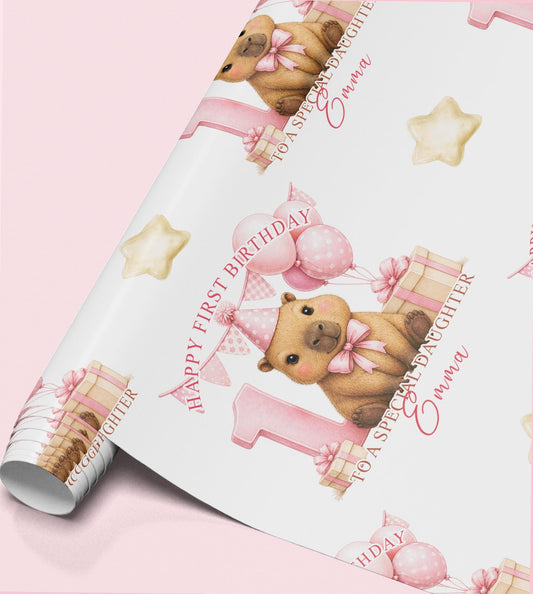 Roll of personalised first birthday wrapping paper featuring a repeating capybara, pink number one and balloon design.