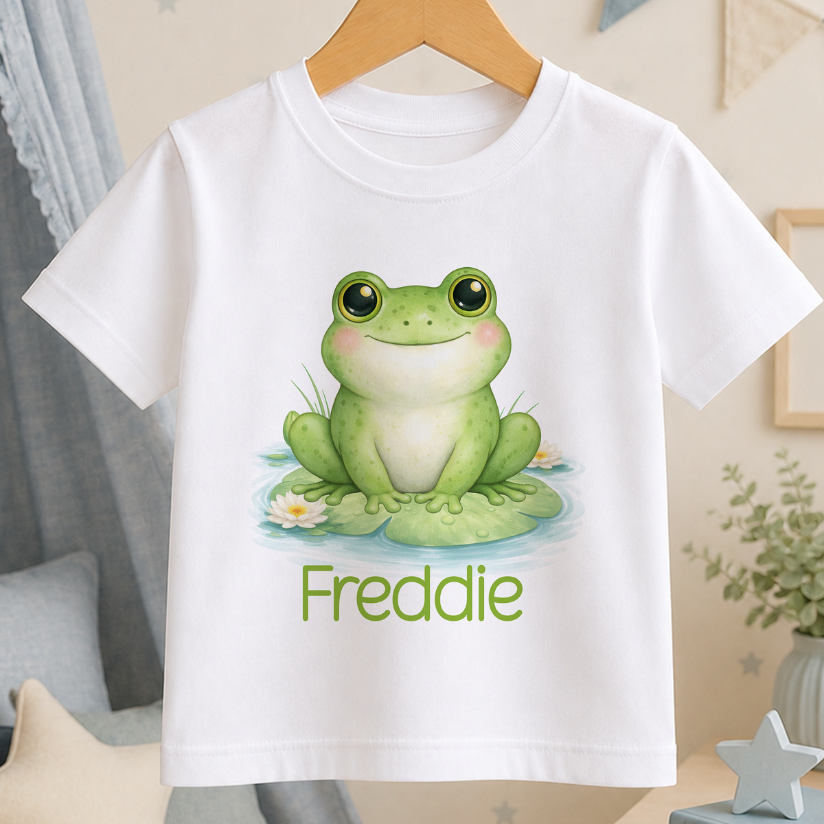 A white t-shirt with a green frog sitting on a lily pad and the name "Freddie" printed below it.