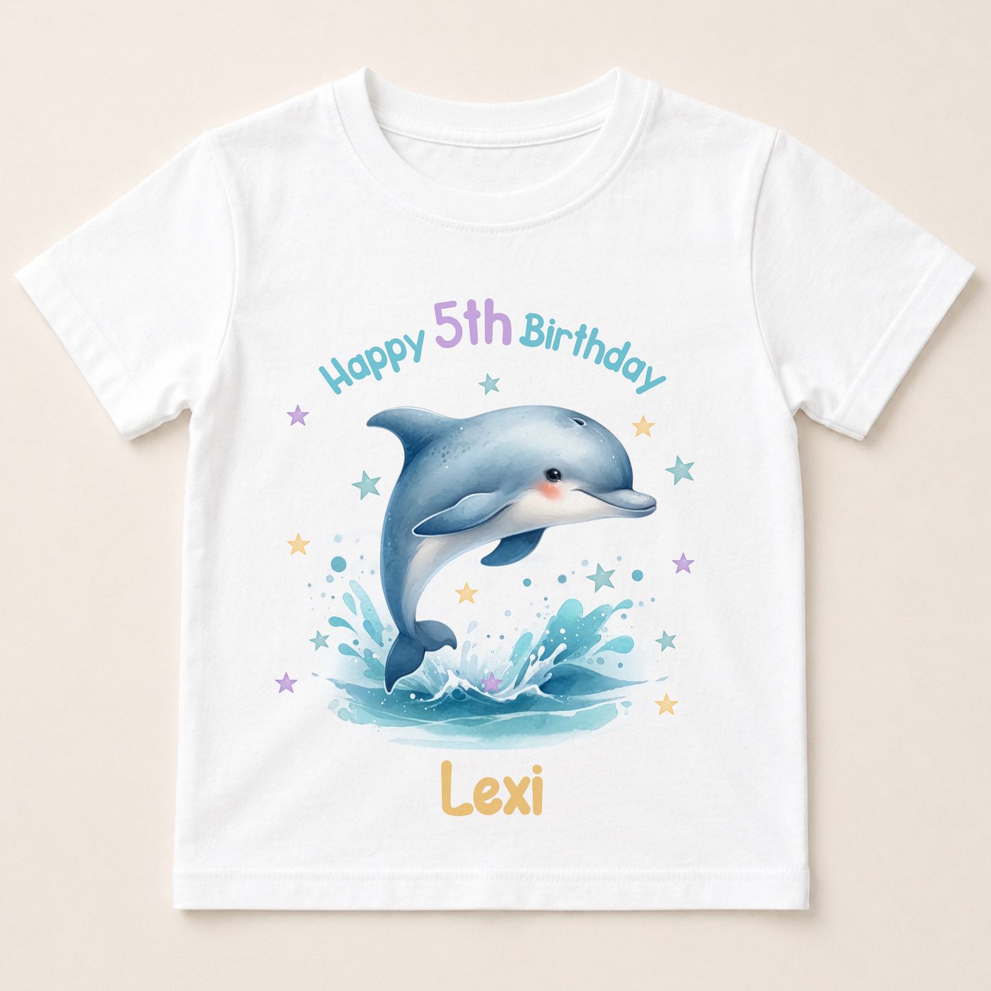 A white t-shirt with a printed design of a dolphin jumping out of the water, surrounded by stars and splashes of water. The text "Happy 5th Birthday Lexi" is displayed above the dolphin.