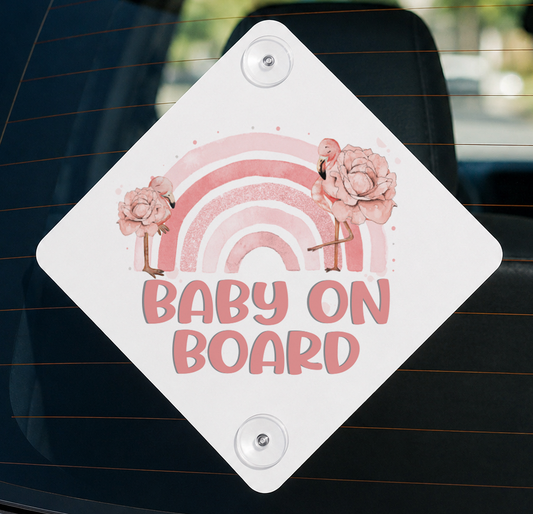 Diamond-shaped white Baby on Board car window sign with pink watercolour flamingos and rainbow, mounted with suction cups on a car window