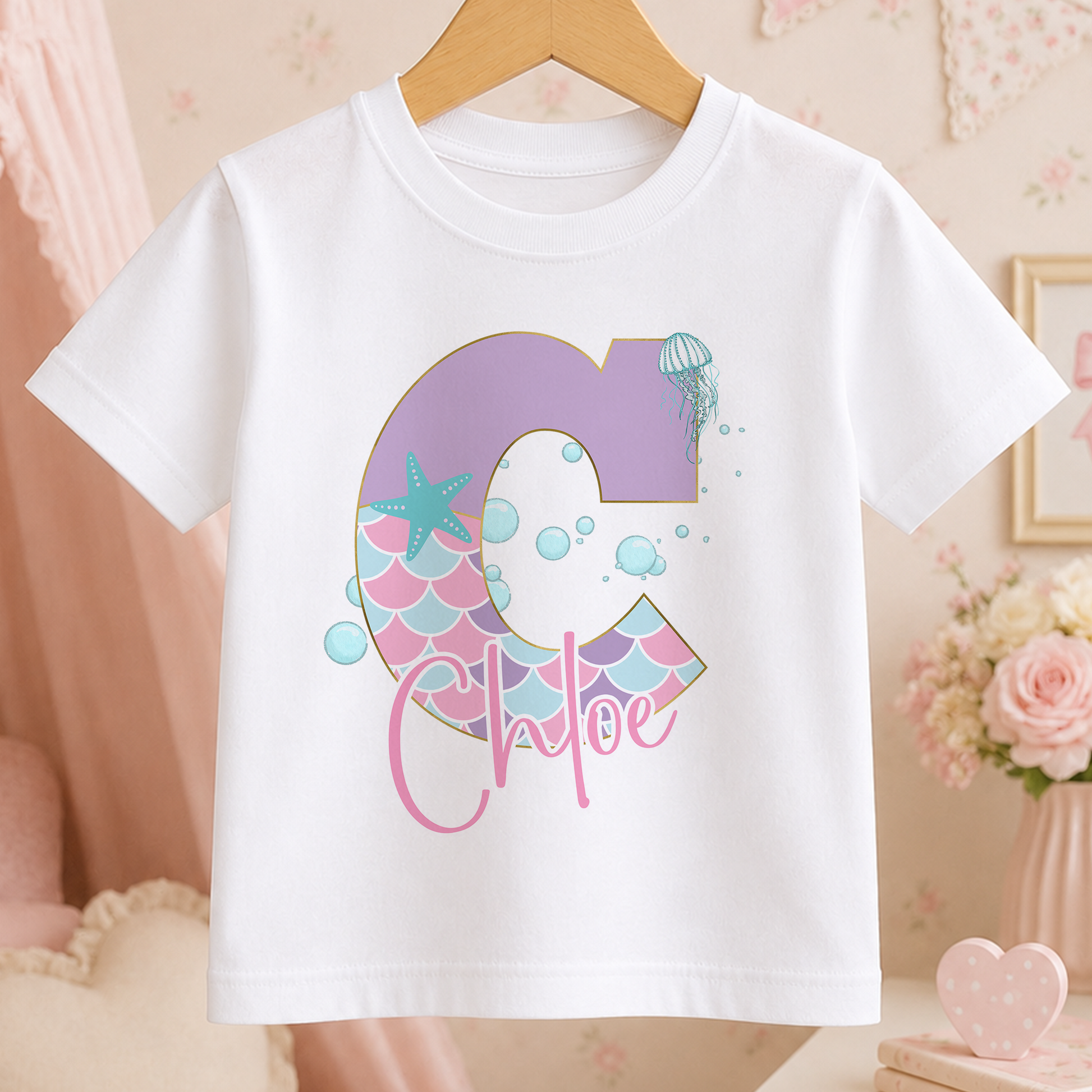 A white t-shirt with a personalized name printed on it, featuring a letter 'C' with a mermaid design and bubbles.