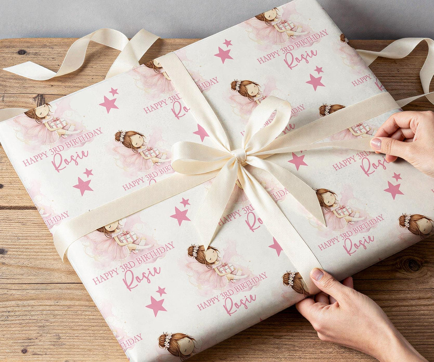 Gift being wrapped in personalised pink fairy birthday wrapping paper with a white ribbon bow.