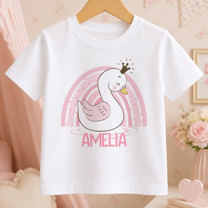 A white t-shirt with a cartoon swan wearing a crown and the name "Amelia" printed on it, along with a rainbow graphic.