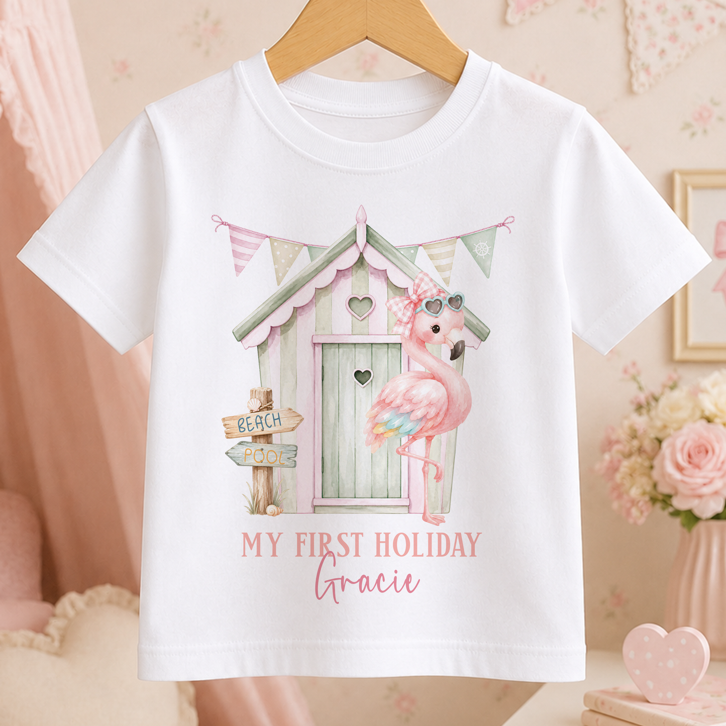 A white t-shirt with a pink flamingo and a beach house graphic, along with the text "My first holiday Gracie".