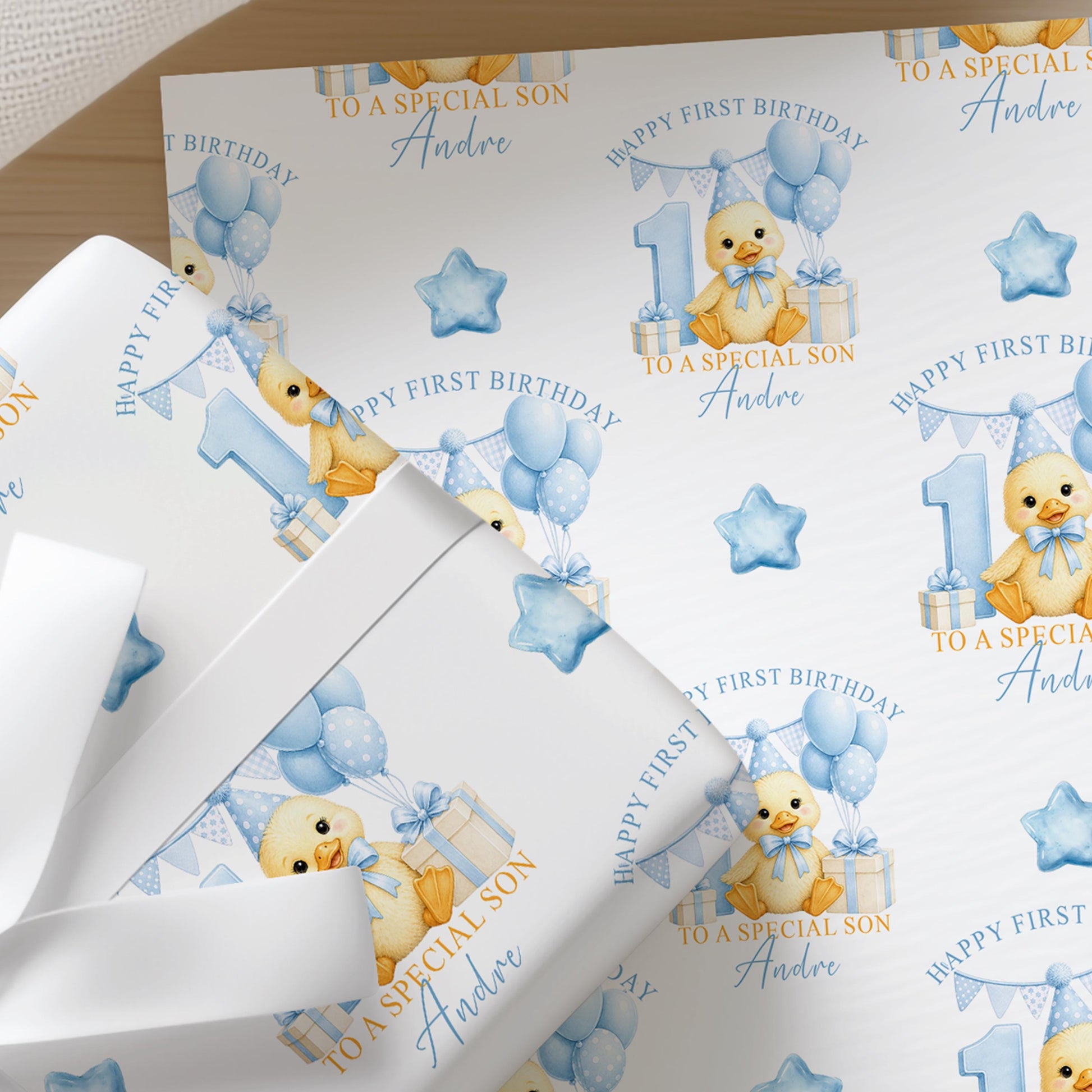 Close-up of personalised first birthday wrapping paper featuring a cute duckling, blue number one, balloons and presents on premium white wrapping paper.