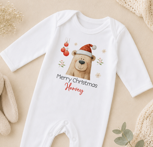 A white onesie with a cartoon bear wearing a Santa hat and the text "Merry Christmas Harvey" printed on it.