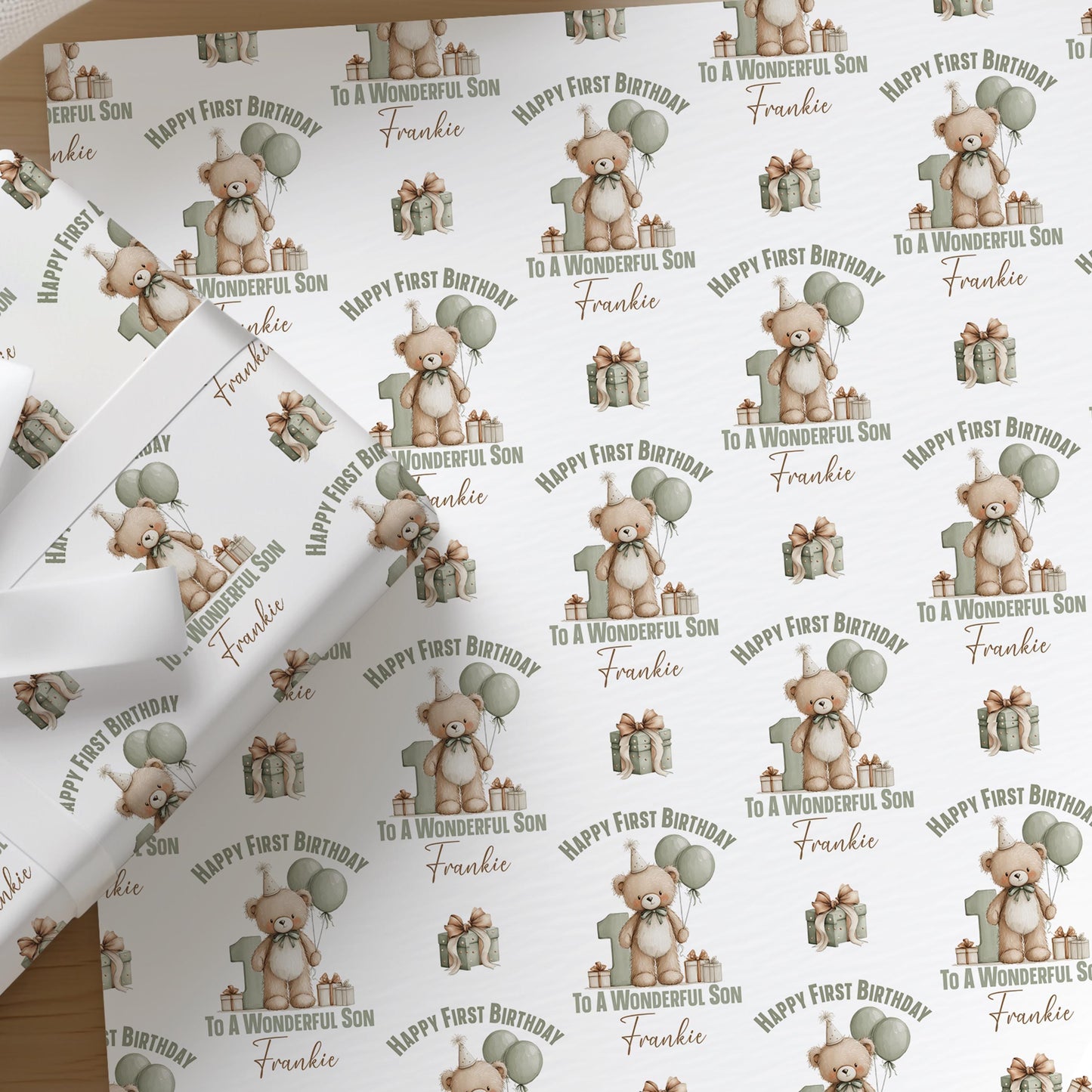 Close-up of personalised teddy bear first birthday wrapping paper for a son, showing the custom printed name among green balloons.