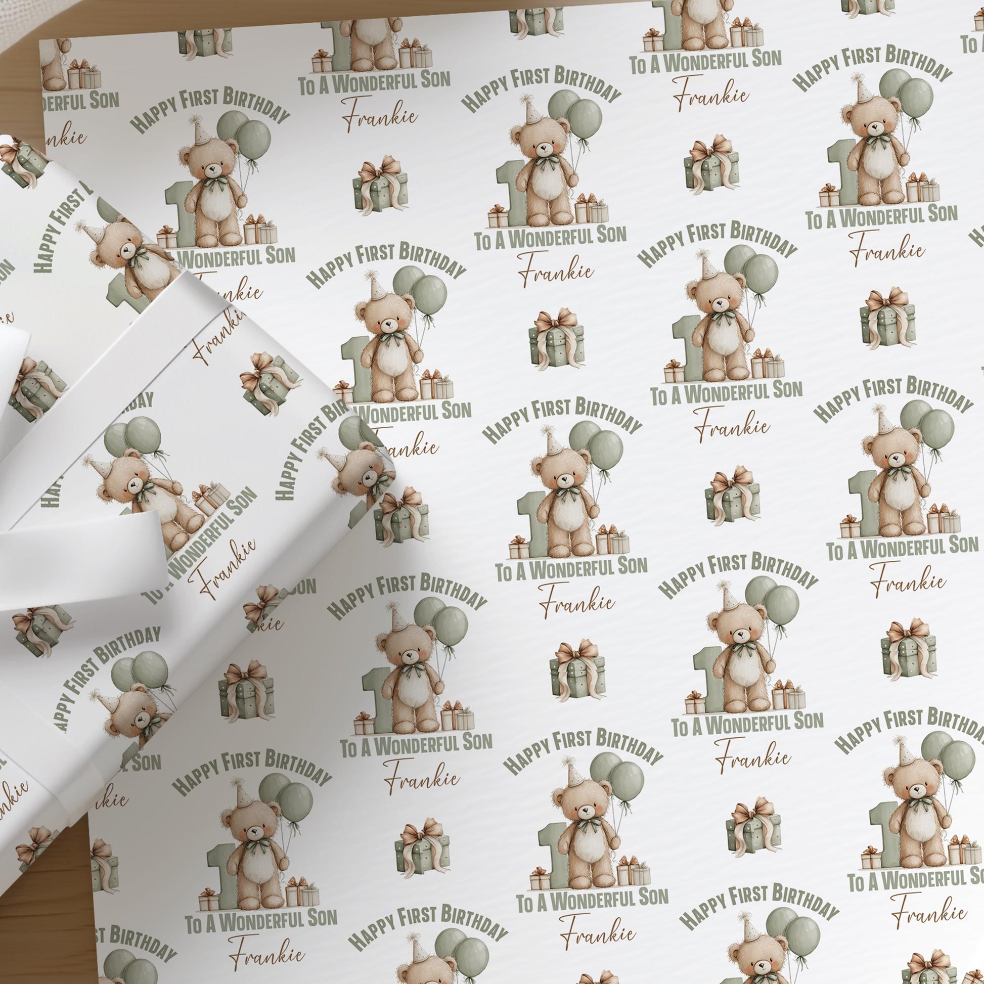 Close-up of personalised teddy bear first birthday wrapping paper for a son, showing the custom printed name among green balloons.
