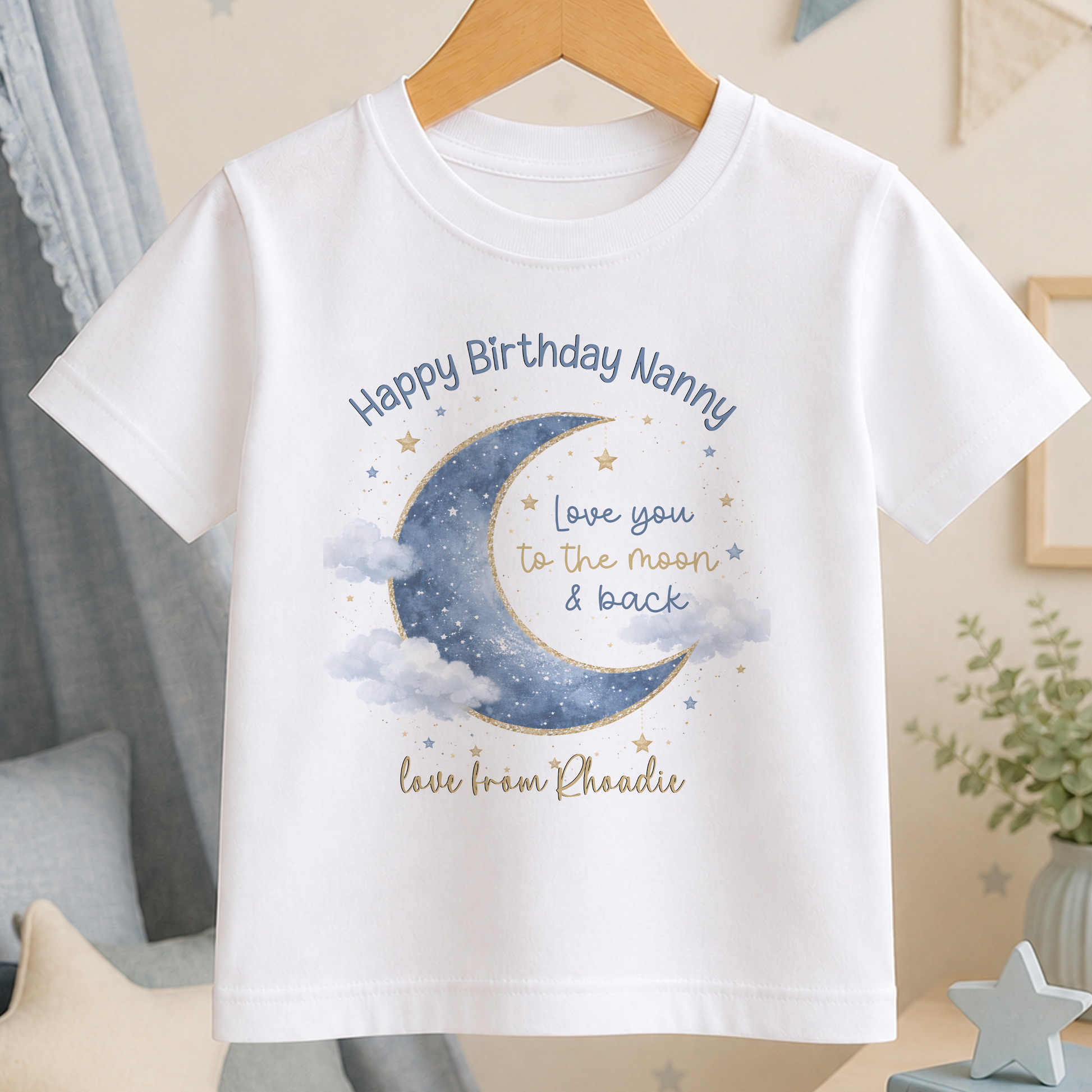 A white t-shirt with a graphic design featuring a crescent moon, stars, and clouds, along with the text "Happy Birthday Nanny" and "Love you to the moon & back" printed on it.
