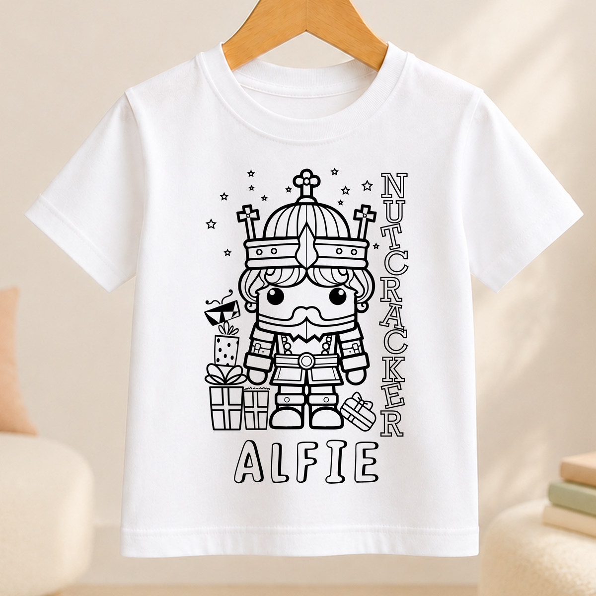 A white t-shirt with a black and white illustration of a nutcracker character wearing a crown and holding a gift box. The text "ALFIE" is written below the illustration.
