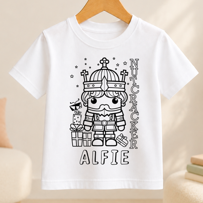 A white t-shirt with a black and white illustration of a nutcracker character wearing a crown and holding a gift box. The text "ALFIE" is written below the illustration.