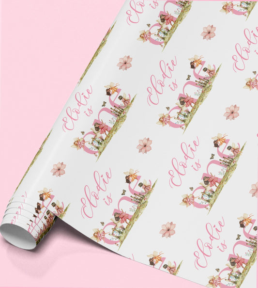 The image is a roll of wrapping paper with a repeating pattern of pink flowers and the text "Ella is" printed on it.