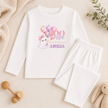 A white long-sleeved shirt with a Halloween-themed graphic, a pair of white pajama pants, and some stuffed animals on a beige background.