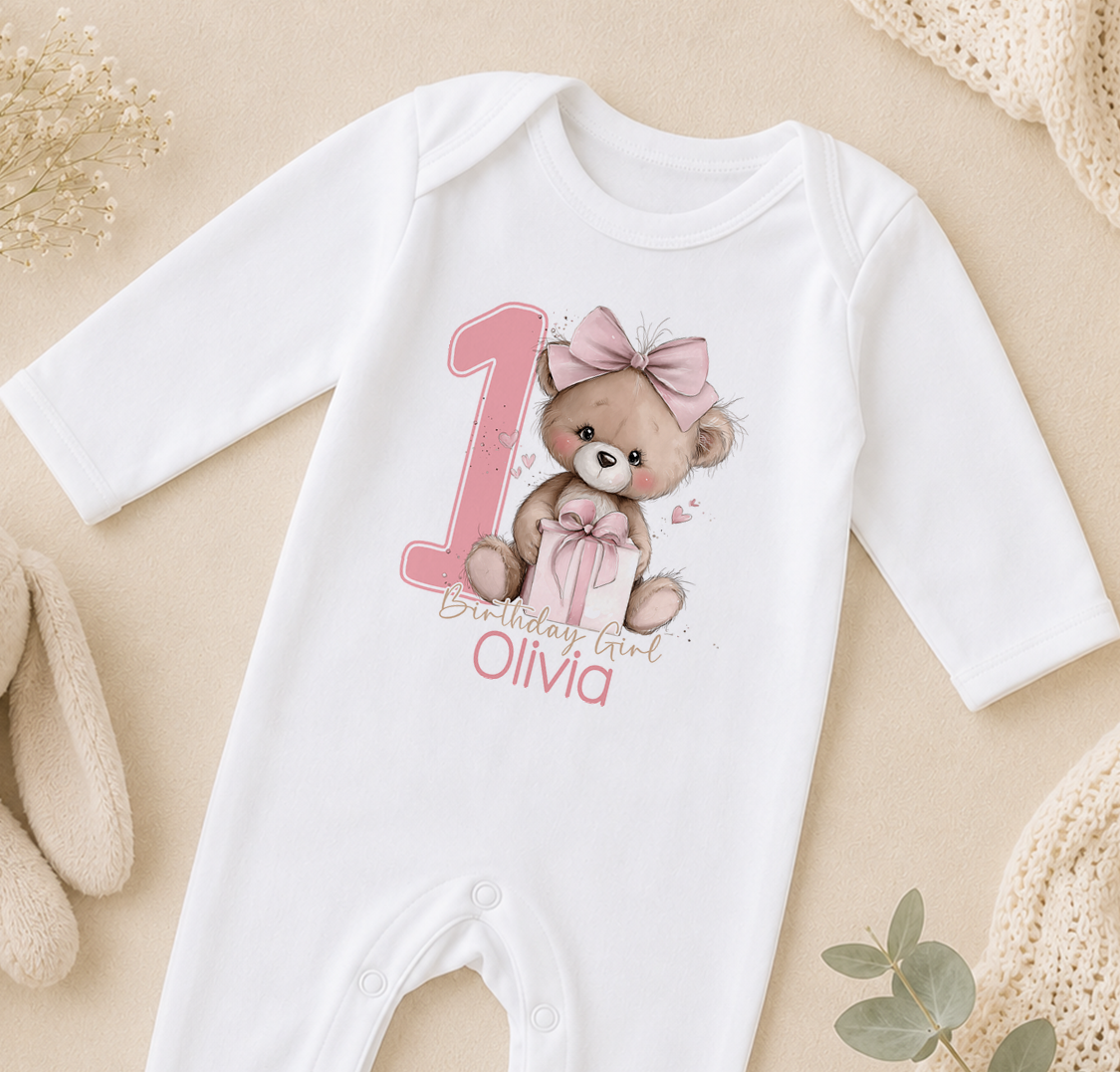 Pink teddy bear first birthday design shown on a personalised baby vest with custom name.