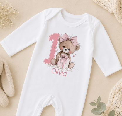 Pink teddy bear first birthday design shown on a personalised baby vest with custom name.
