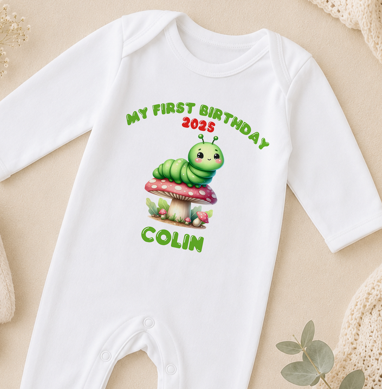 A white onesie with a cartoon caterpillar and the text "My first birthday 2015 COLIN" printed on it.