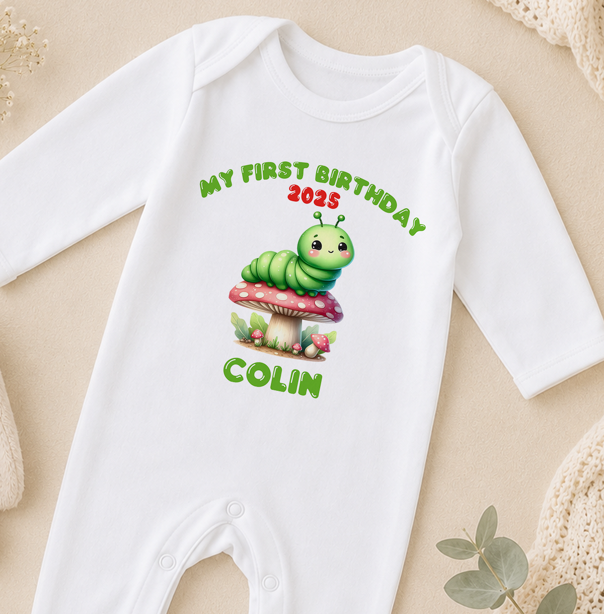 A white onesie with a cartoon caterpillar and the text "My first birthday 2015 COLIN" printed on it.