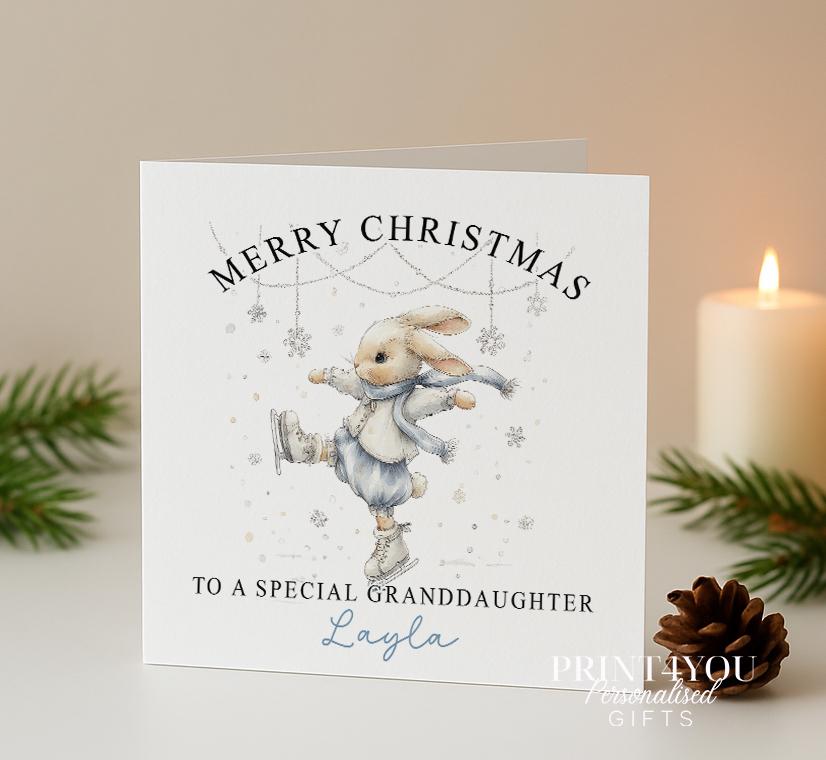 Personalised Christmas card front showing a blue watercolour bunny ice skating, with custom name and relation text example