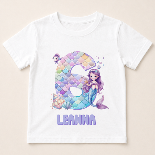 A white t-shirt with a design featuring a mermaid character and the number 6.