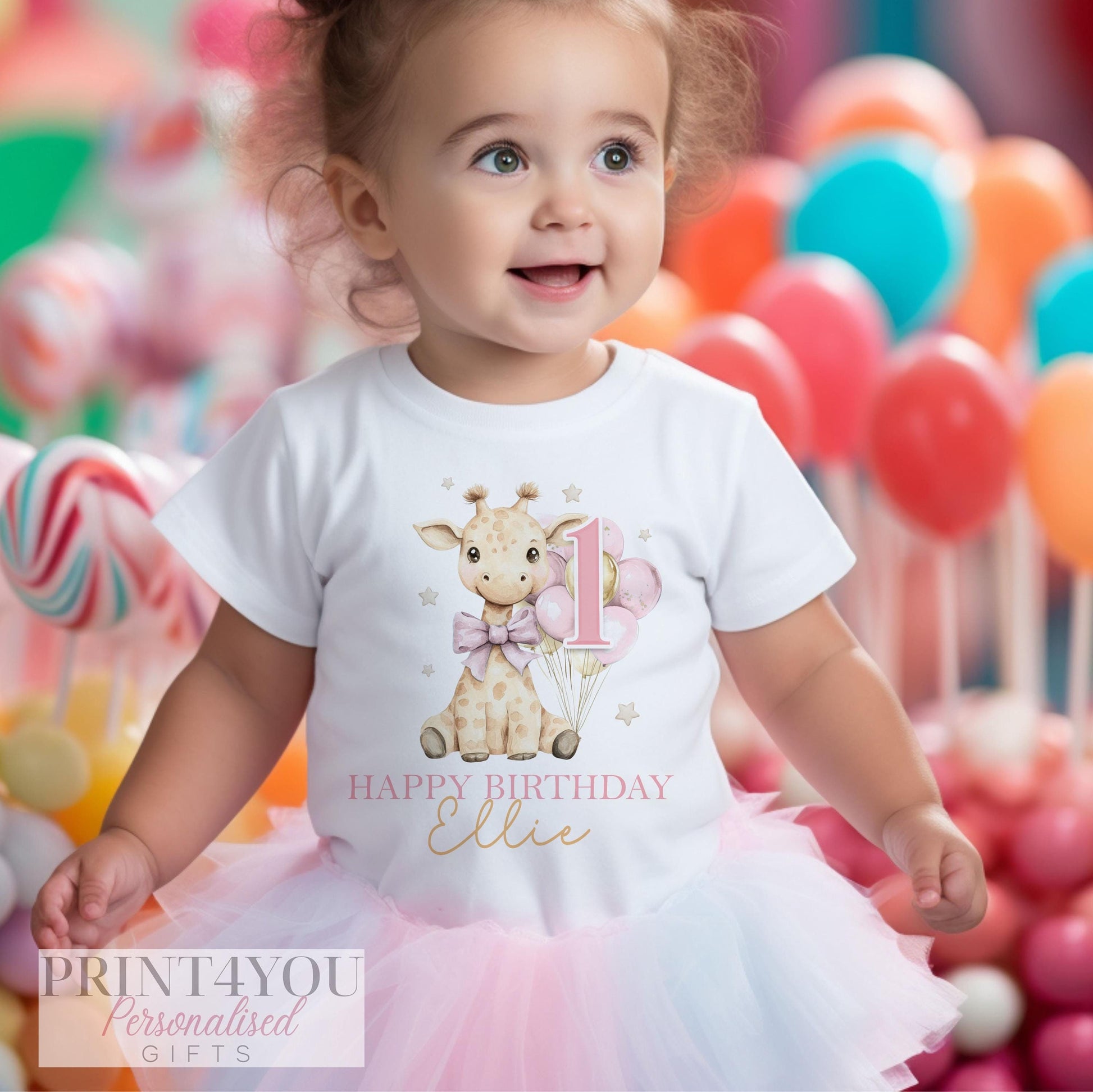 a one year old toddler wearing a white t-shirt printed with a cute giraffe holding pink and gold balloons. There is text reading Happy Birthday and a name, and a large pink number one.