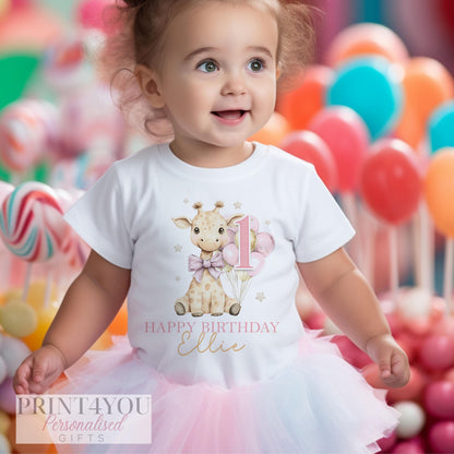 a one year old toddler wearing a white t-shirt printed with a cute giraffe holding pink and gold balloons. There is text reading Happy Birthday and a name, and a large pink number one.