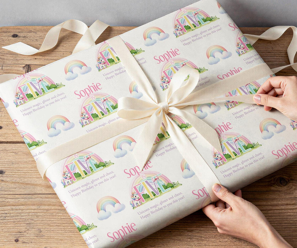 Hands wrapping a gift in personalised unicorn and rainbow wrapping paper printed with the name Sophie.