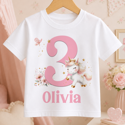 A white t-shirt with a pink unicorn and the number 3 printed on it, along with the name "Olivia" below the number.