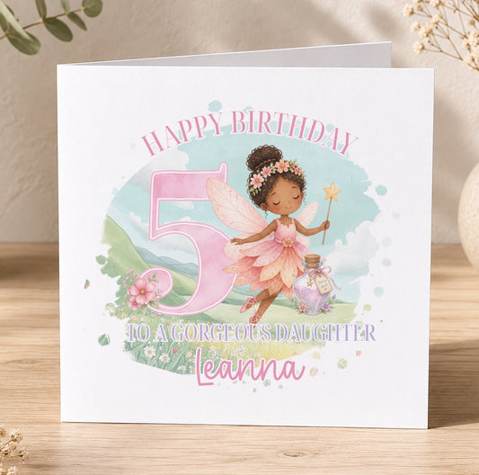 Personalised fairy birthday card showing a brown-skinned fairy with wings and a flower crown beside a pink number, with the printed message 'Happy Birthday to a Gorgeous Daughter', shown here with the example name Leanna.