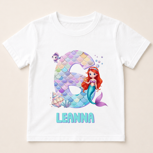 A white t-shirt with a design featuring a mermaid character and the number 6.