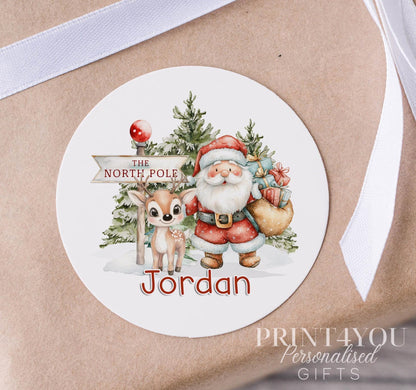 Personalised Santa and reindeer Christmas sticker in a fun winter colour palette, custom name printed on a glossy round gift label strip