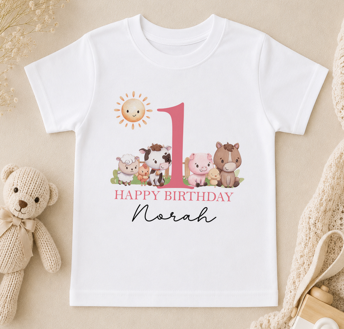 A white t-shirt with a graphic design featuring a large number 1 surrounded by various animals, including a cow, pig, and sheep, along with the text "Happy Birthday Noah".