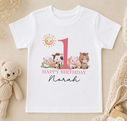 A white t-shirt with a graphic design featuring a large number 1 surrounded by various animals, including a cow, pig, and sheep, along with the text "Happy Birthday Noah".