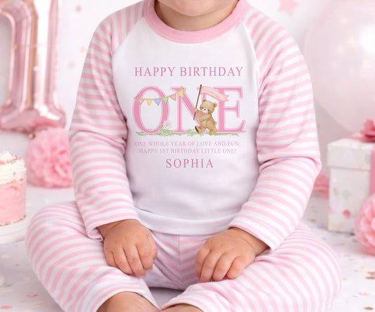 Personalised first birthday pyjamas in a pink striped design with the baby's name printed on the front.
