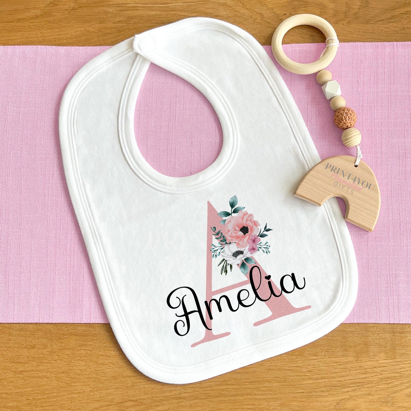 Personalised baby vest in white cotton, printed with soft pink flowers surrounding a custom initial.
