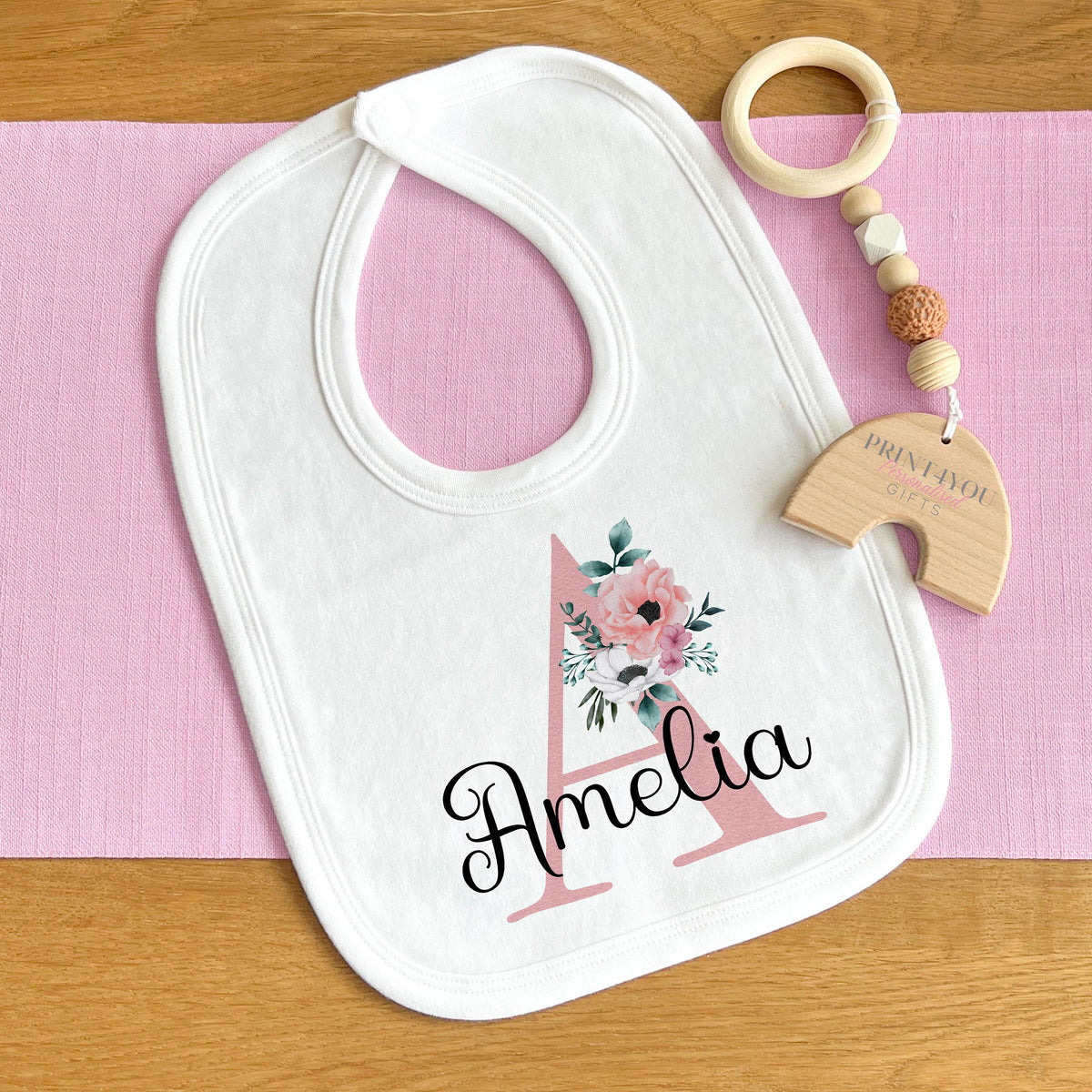 Personalised baby vest in white cotton, printed with soft pink flowers surrounding a custom initial.