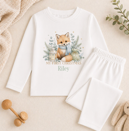 A white long-sleeved shirt with a printed image of a fox and Christmas decorations, along with a pair of white pajama pants, a stuffed animal, and some decorative elements.