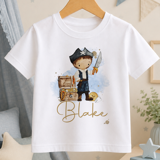A white t-shirt with a pirate-themed graphic design, including a cartoon pirate character and a treasure chest. The name " Blake" is written below the graphic.