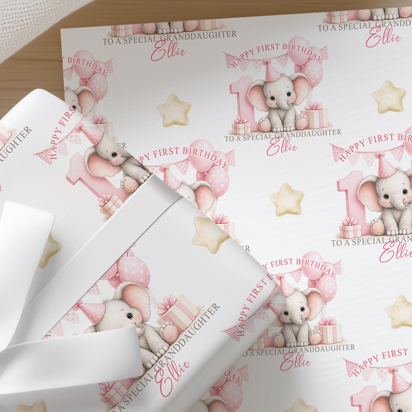 Close-up of personalised first birthday wrapping paper featuring a cute baby elephant, pink number one, balloons and presents on premium white wrapping paper.