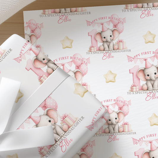 Close-up of personalised first birthday wrapping paper featuring a cute baby elephant, pink number one, balloons and presents on premium white wrapping paper.