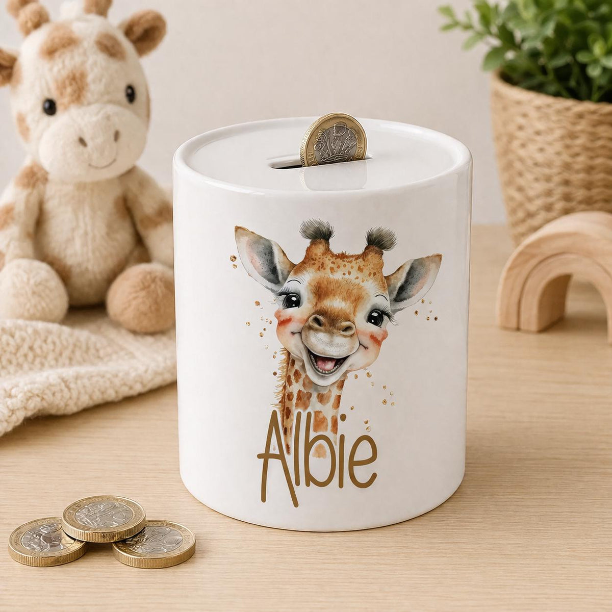 White ceramic money box personalised with the name Albie, printed with a smiling baby giraffe face illustration and gold sparkle details