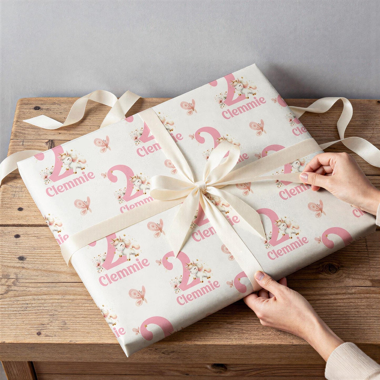 Hands wrapping a gift in personalised pink and white wrapping paper printed with the name 'Clemmie' and age '2'