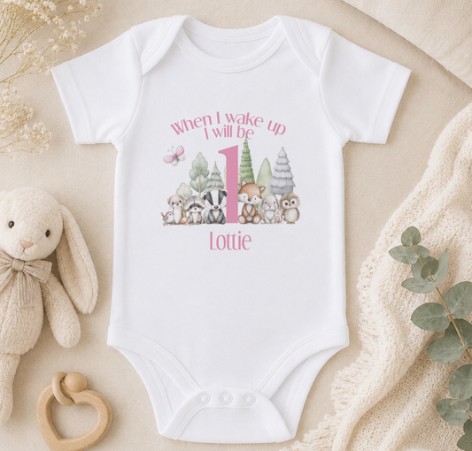 A white onesie with a personalized print of woodland animals and the text "When I wake up I will be Lottie" printed on it, along with a rabbit and a teddy bear.