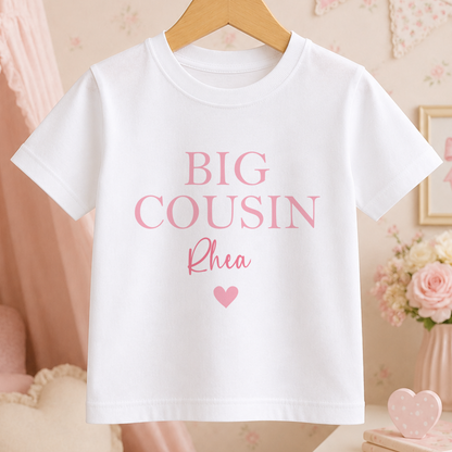 A white t-shirt with the text "BIG COUSIN Rhea" printed on it, along with a heart symbol.