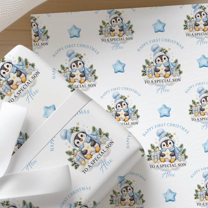 Flat sheets of personalised penguin baby first Christmas wrapping paper with a blue star gift box