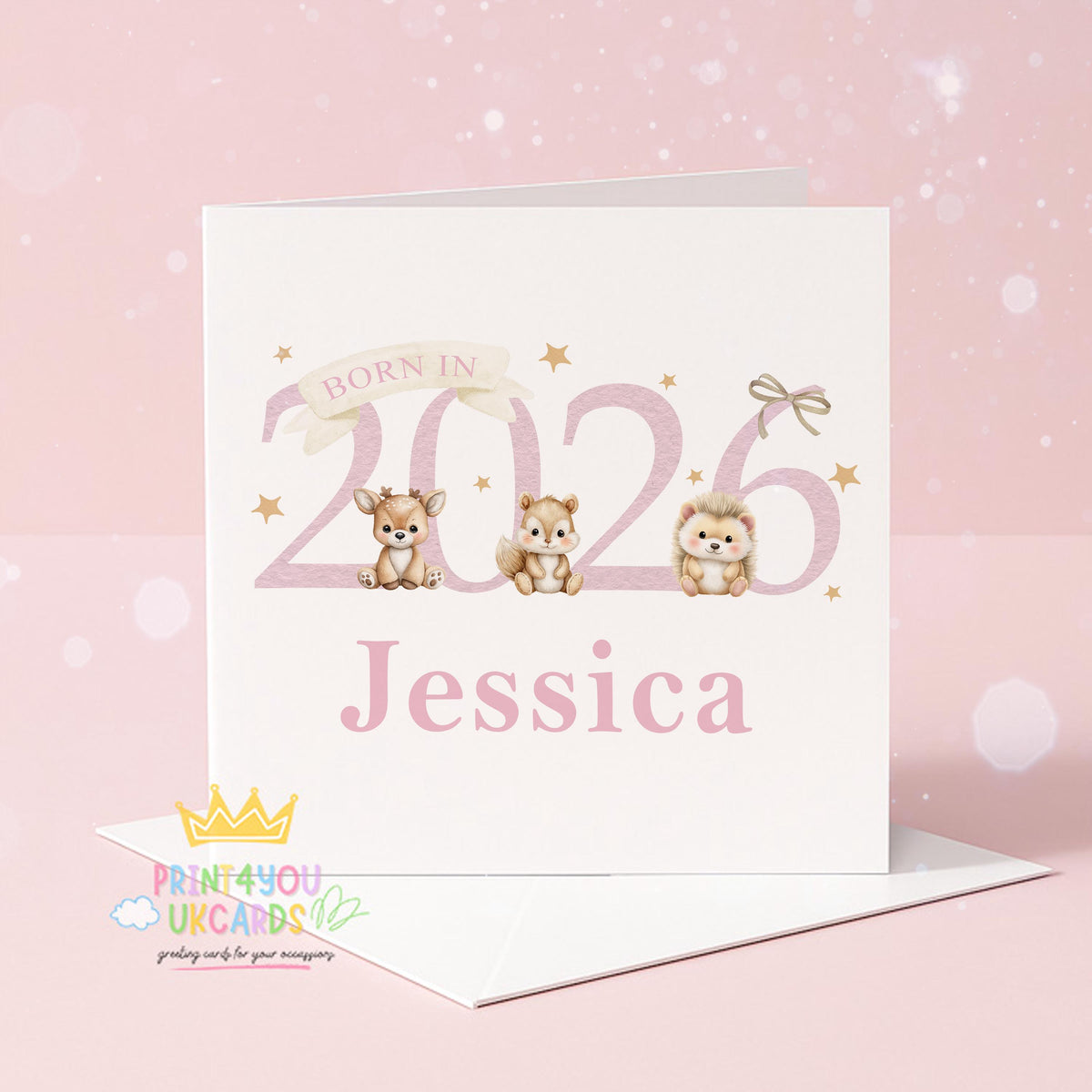 White square newborn card standing on a wooden surface with eucalyptus leaves, reading 'Born In 2026' with an illustrated deer, chipmunk and hedgehog, personalised with the name Jessica