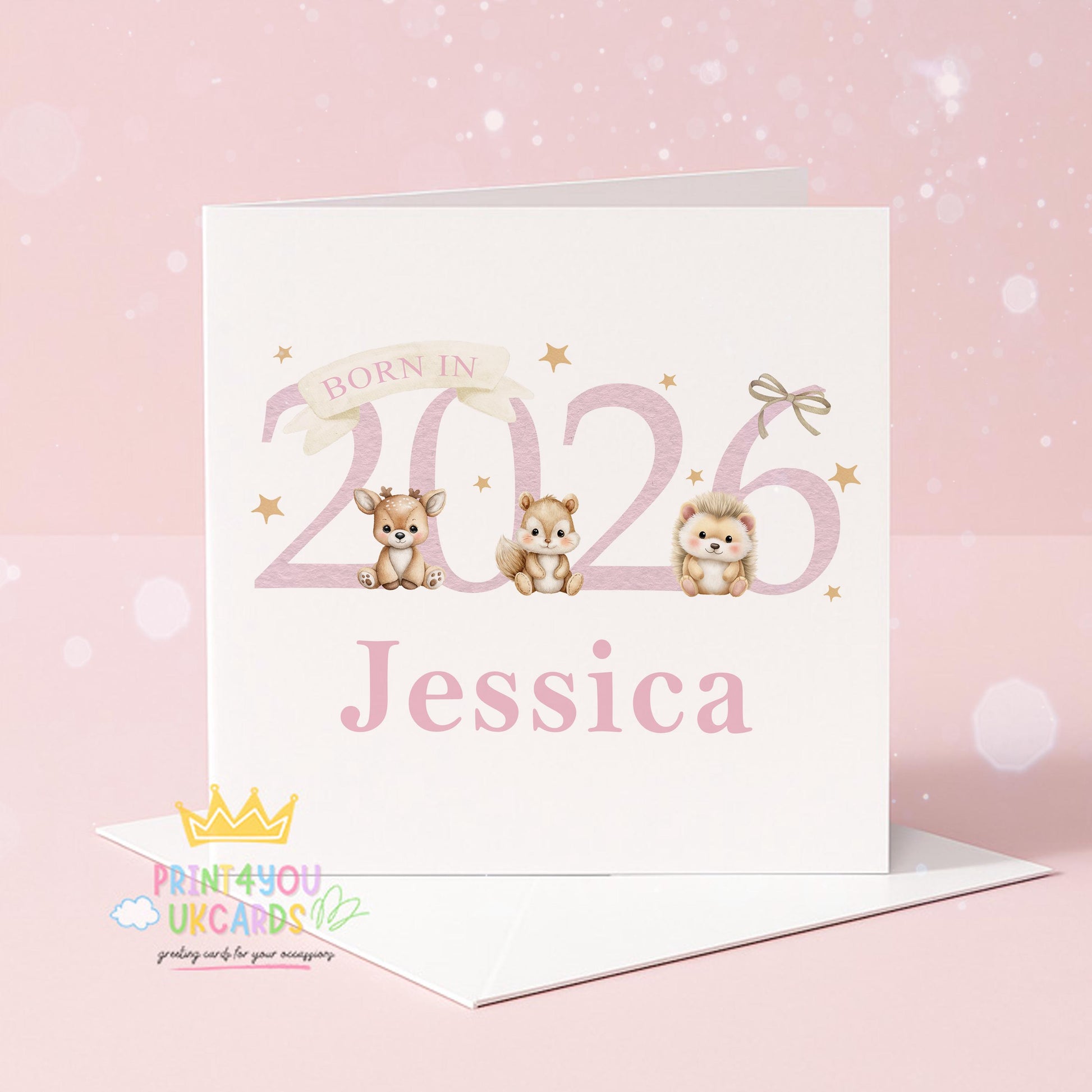 White square newborn card standing on a wooden surface with eucalyptus leaves, reading 'Born In 2026' with an illustrated deer, chipmunk and hedgehog, personalised with the name Jessica