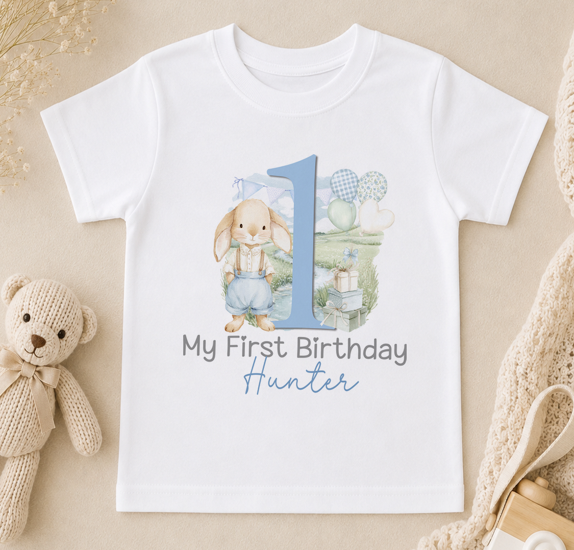 White t-shirt printed with a bunny design, a blue number one and 'My First Birthday' with a personalised name underneath.